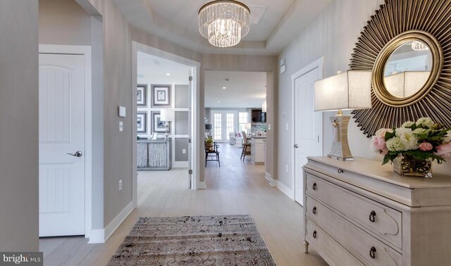 hall with a raised ceiling, a chandelier, and light hardwood / wood-style floors