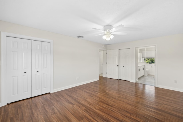 unfurnished bedroom featuring wood finished floors, baseboards, two closets, connected bathroom, and ceiling fan