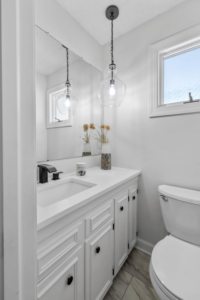 half bathroom featuring vanity, toilet, marble look tiles, and baseboards