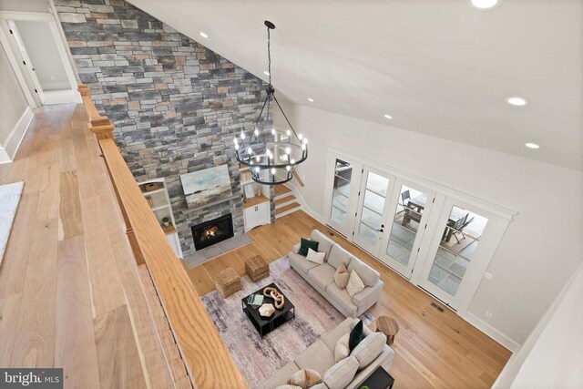  - living room featuring wood finished floors, vaulted ceiling, a stone fireplace, baseboards, and a chandelier