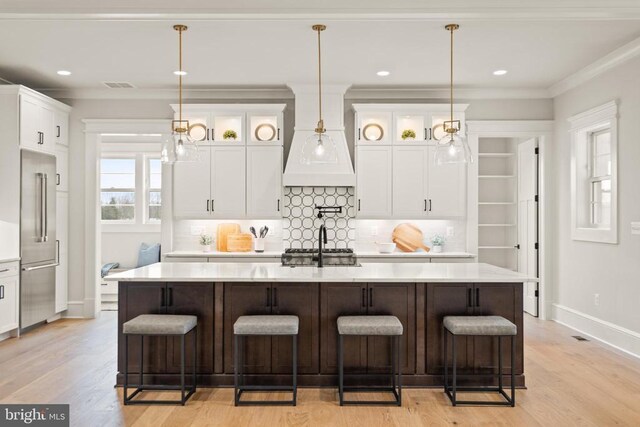  - kitchen with high quality fridge, baseboards, light wood-style floors, light countertops, and a center island with sink