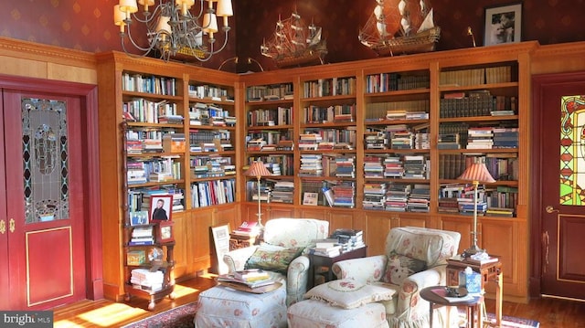  - sitting room with wood finished floors, wall of books, and wallpapered walls