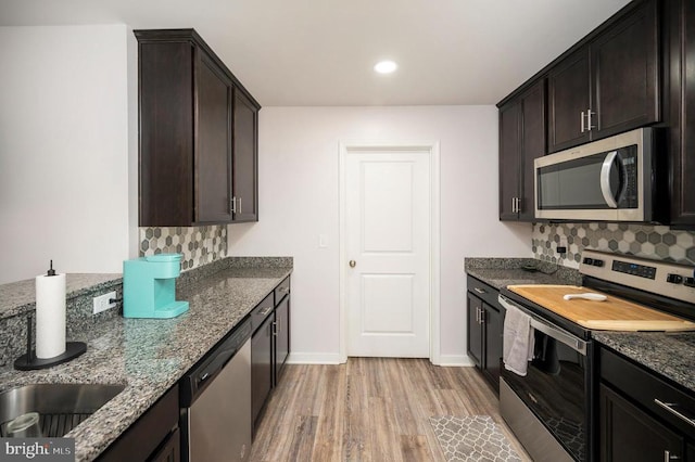 kitchen featuring appliances with stainless steel finishes, light wood-style flooring, dark stone countertops, baseboards, and dark brown cabinets