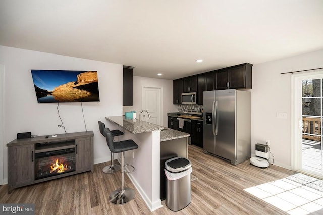 kitchen with stainless steel appliances, light wood-style flooring, baseboards, light stone counters, and a breakfast bar