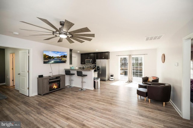 living area featuring light wood-style flooring, a ceiling fan, baseboards, and a lit fireplace