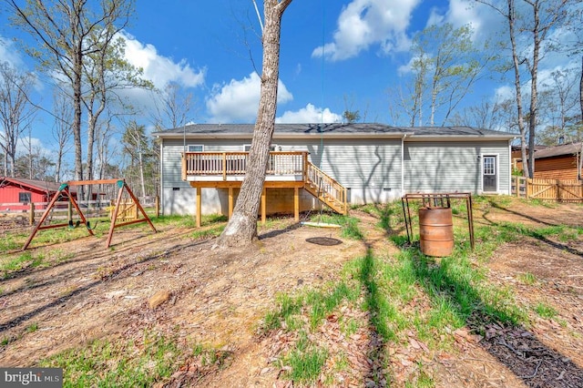 rear view of property with a deck, a playground, crawl space, fence, and stairway