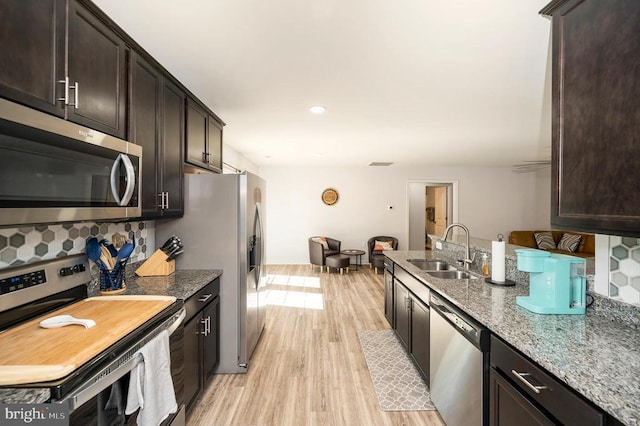 kitchen featuring appliances with stainless steel finishes, a sink, light wood-type flooring, dark brown cabinetry, and recessed lighting