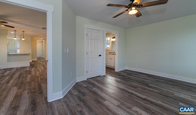 unfurnished bedroom with multiple windows, dark wood finished floors, ensuite bath, and baseboards