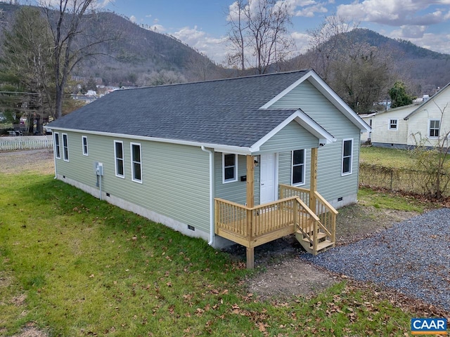 rear view of house featuring a shingled roof, a mountain view, crawl space, and a lawn