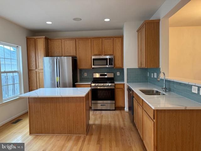 kitchen featuring appliances with stainless steel finishes, a sink, light wood-style flooring, tasteful backsplash, and a center island