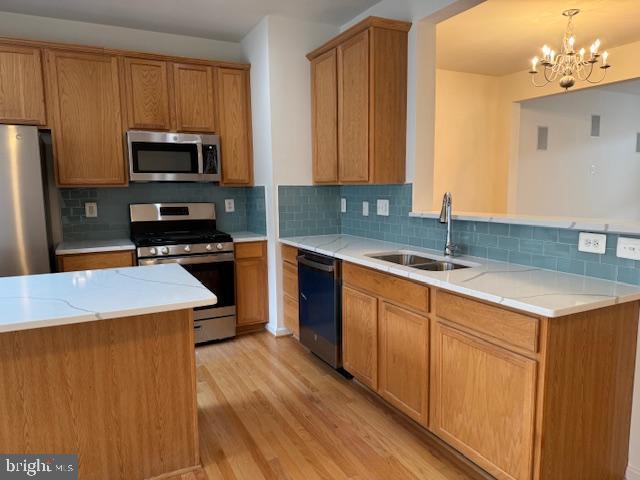 kitchen with stainless steel appliances, a sink, light wood-style floors, a chandelier, and tasteful backsplash