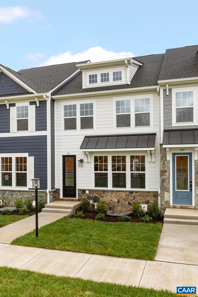 view of property featuring stone siding, a standing seam roof, a shingled roof, and a front yard