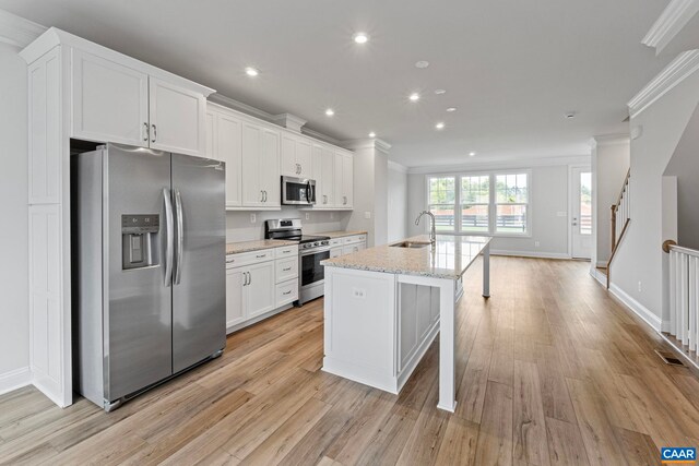 kitchen featuring ornamental molding, a sink, light wood-style floors, a center island with sink, and stainless steel appliances