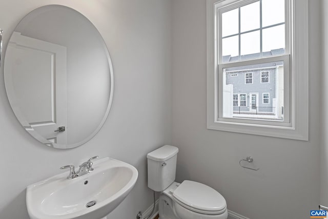 half bath with toilet, baseboards, and a sink