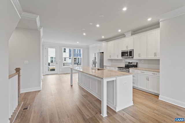 kitchen with ornamental molding, visible vents, white cabinets, stainless steel appliances, and a kitchen island with sink