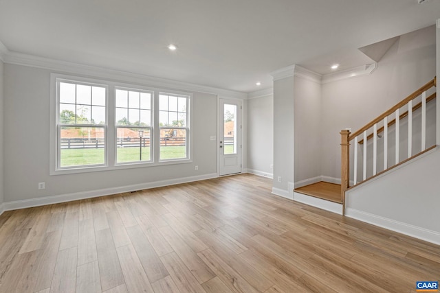 unfurnished living room with crown molding, light wood-type flooring, baseboards, and stairs