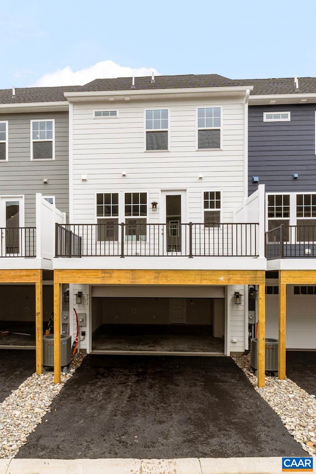 back of house with an attached garage, central AC unit, and aphalt driveway