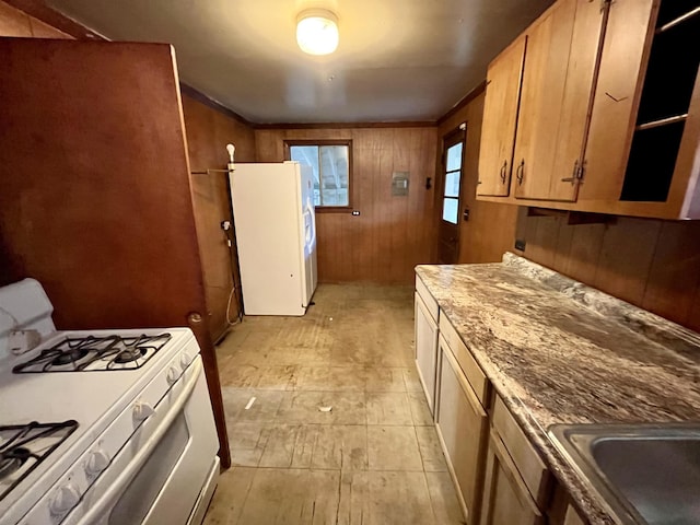 kitchen with white appliances, wooden walls, and a sink