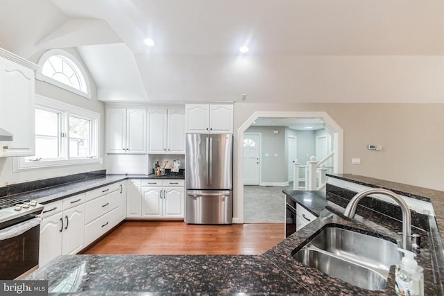 kitchen with stainless steel appliances, a sink, arched walkways, wood finished floors, and dark stone counters