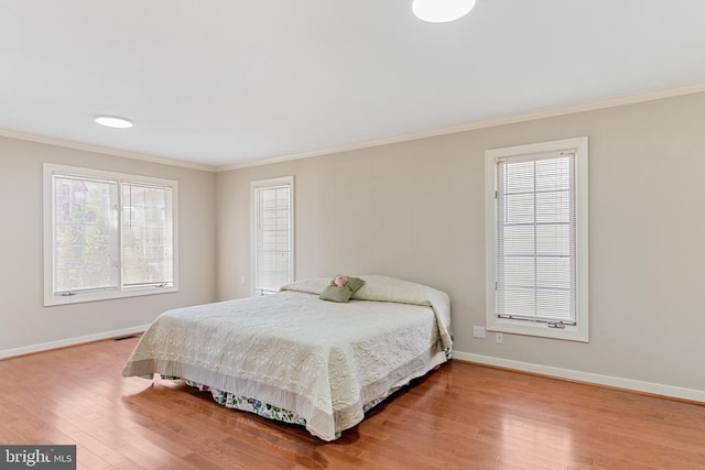 bedroom featuring crown molding, baseboards, wood finished floors, and multiple windows