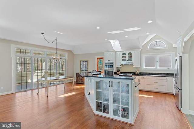 kitchen featuring vaulted ceiling, stainless steel appliances, glass insert cabinets, dark countertops, and white cabinetry