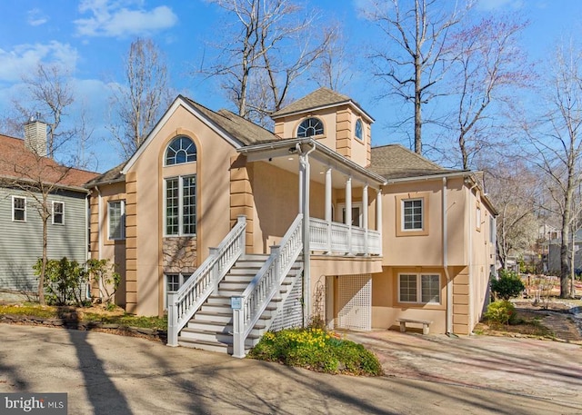 view of front of property with stucco siding, covered porch, stairs, concrete driveway, and a shingled roof
