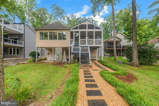 rear view of house with a sunroom, stucco siding, stairs, and a yard