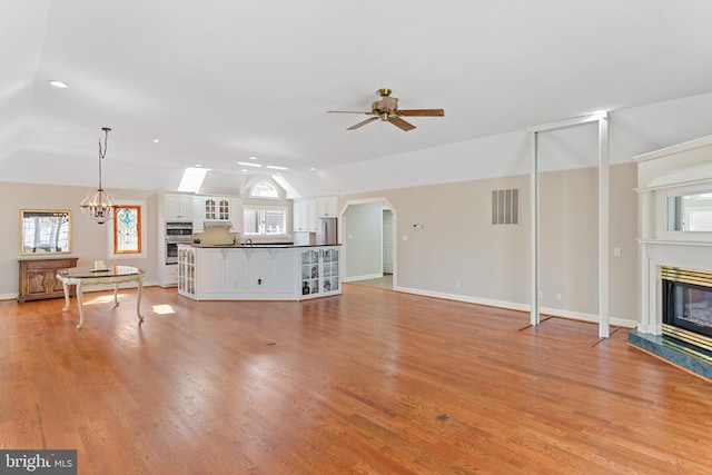 unfurnished living room with lofted ceiling, a fireplace, ceiling fan, healthy amount of natural light, and a chandelier