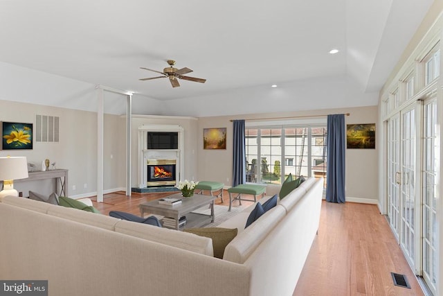living room featuring light wood-type flooring, a glass covered fireplace, baseboards, ceiling fan, and recessed lighting