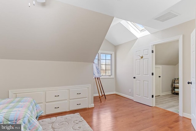 bedroom featuring vaulted ceiling, light wood-style floors, a skylight, and baseboards