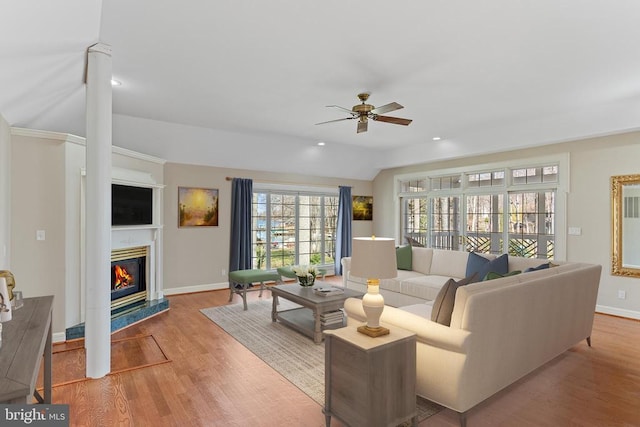living room with a ceiling fan, a glass covered fireplace, wood finished floors, baseboards, and lofted ceiling