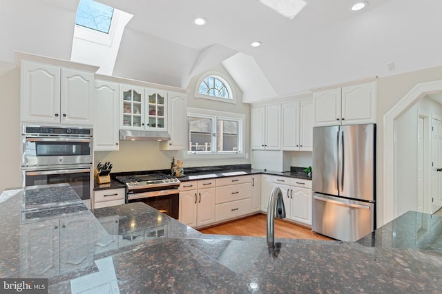 kitchen with stainless steel appliances, a skylight, under cabinet range hood, lofted ceiling, and white cabinets