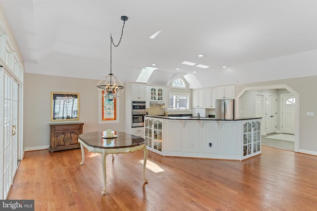 kitchen featuring stainless steel appliances, dark countertops, lofted ceiling, white cabinets, and glass insert cabinets