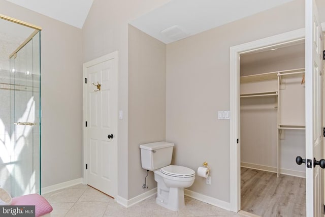 bathroom featuring a stall shower, toilet, vaulted ceiling, a walk in closet, and baseboards