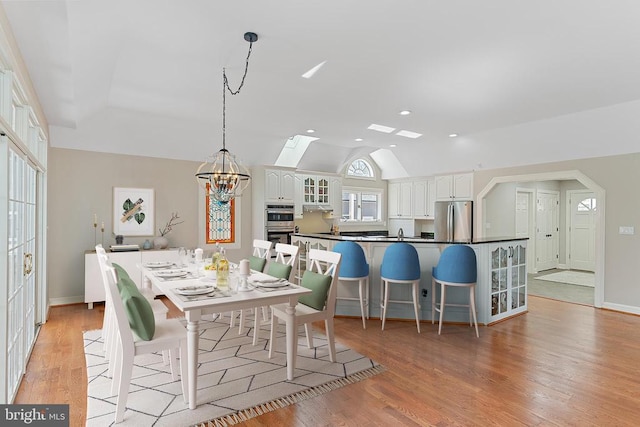 dining room featuring lofted ceiling, light wood finished floors, a chandelier, a skylight, and recessed lighting
