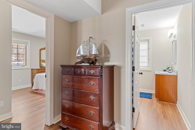 hall featuring light wood finished floors, baseboards, and a sink