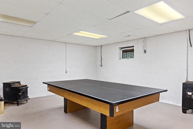 rec room with concrete flooring, concrete block wall, a wood stove, and a drop ceiling