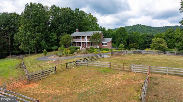 view of front of house with a forest view, fence, a front lawn, and a rural view