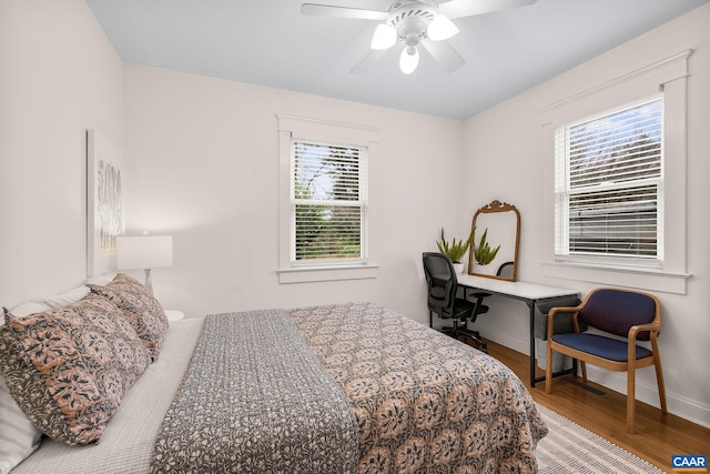 bedroom featuring wood finished floors, baseboards, a ceiling fan, and multiple windows