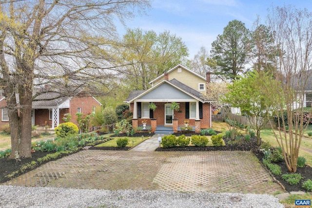 bungalow featuring a chimney, a porch, brick siding, and fence