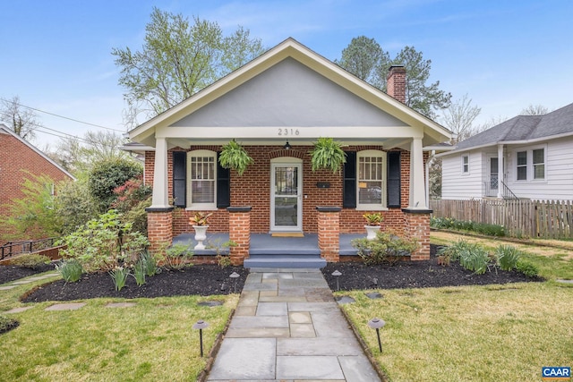 bungalow-style home featuring fence, a front yard, a chimney, and brick siding