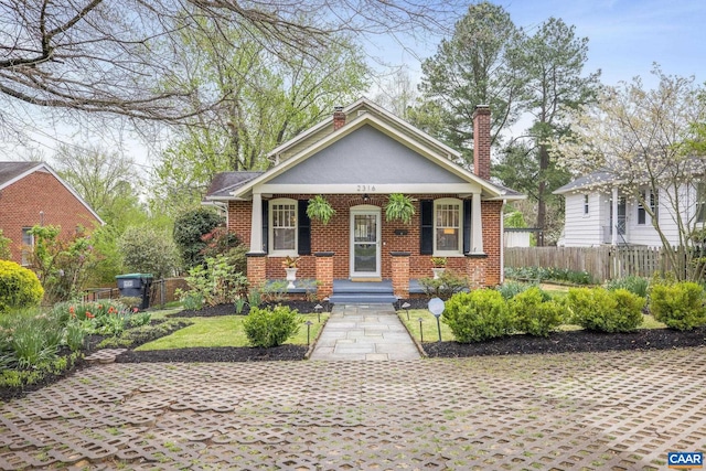 bungalow featuring covered porch, stucco siding, a chimney, fence, and brick siding