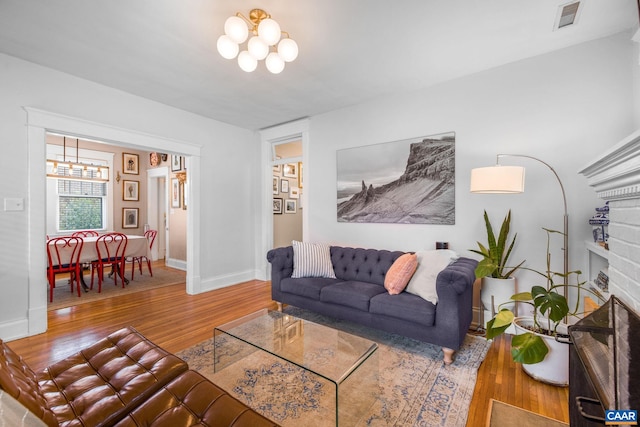 living room with baseboards, an inviting chandelier, visible vents, a brick fireplace, and wood finished floors