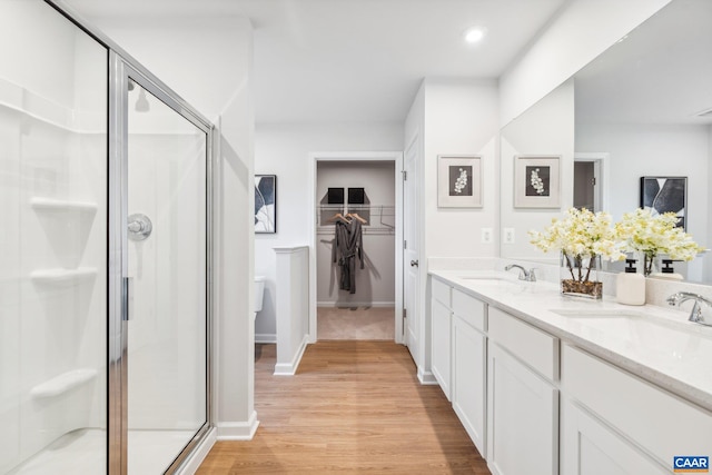 full bath featuring a stall shower, a sink, double vanity, a walk in closet, and wood finished floors