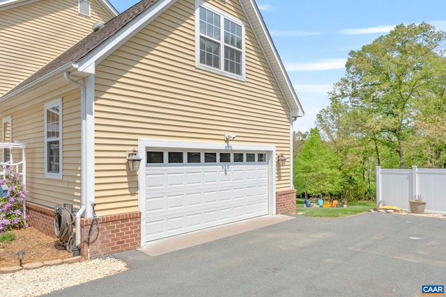 view of home's exterior featuring asphalt driveway, brick siding, fence, and a garage