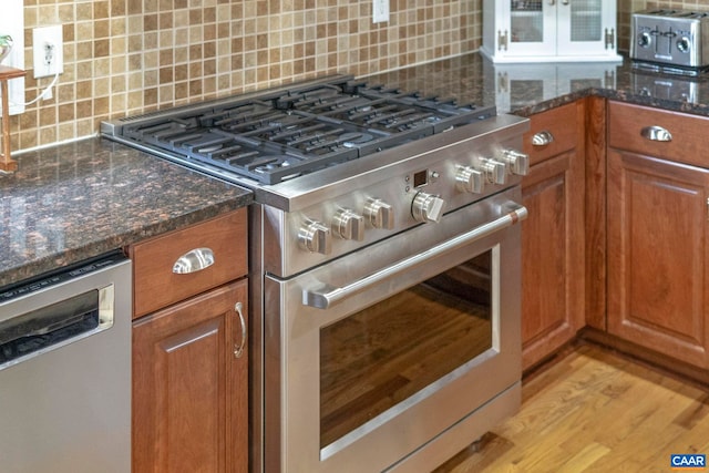 kitchen featuring appliances with stainless steel finishes, brown cabinets, tasteful backsplash, dark stone counters, and light wood-style floors