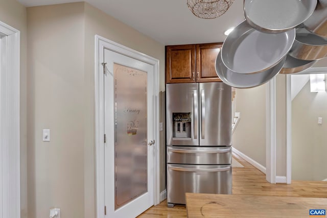 kitchen with stainless steel fridge with ice dispenser, light wood-type flooring, baseboards, and brown cabinetry