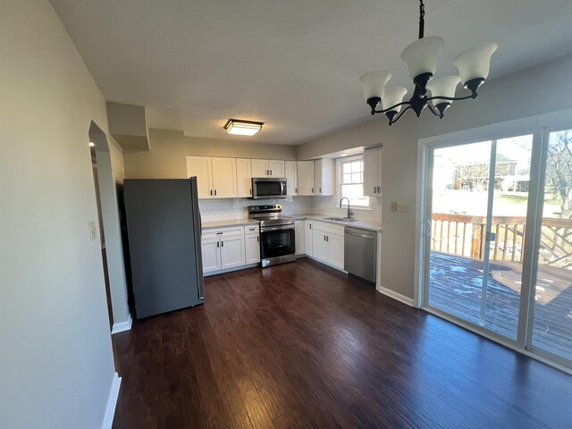 kitchen with sink, dark wood-type flooring, appliances with stainless steel finishes, white cabinetry, and backsplash