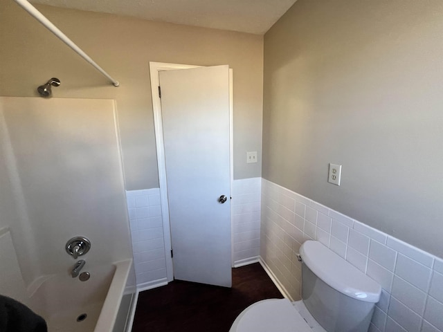 bathroom featuring tile walls, toilet, and washtub / shower combination