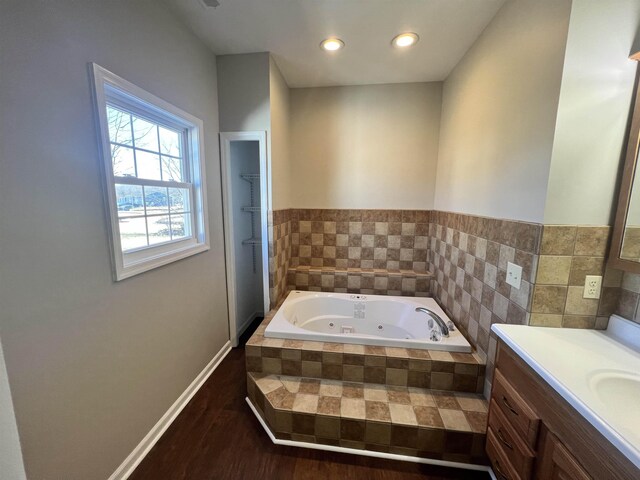 bathroom featuring hardwood / wood-style flooring, vanity, and tiled bath